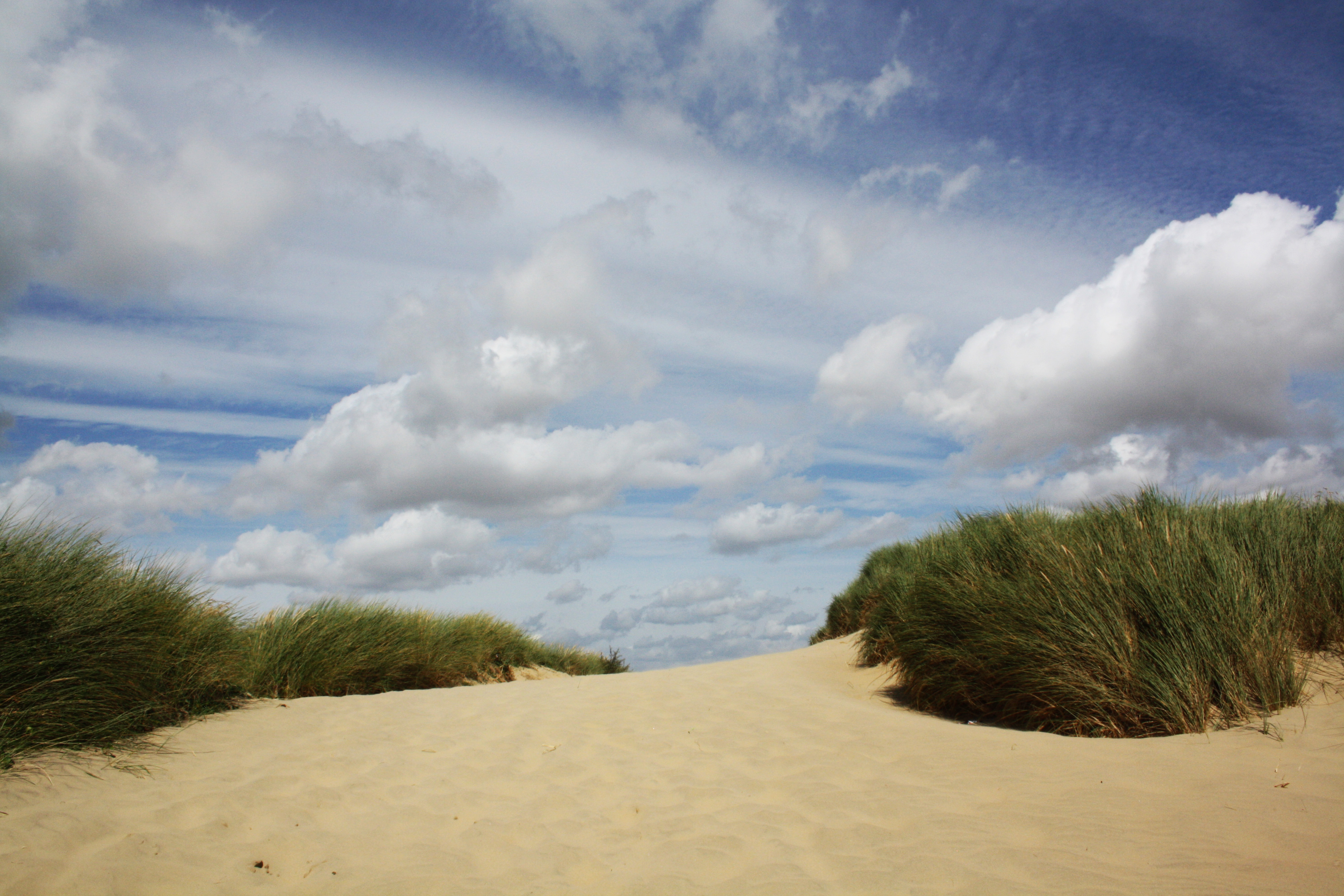 Camber Sands beach sand dune with blue sky and white clouds.
